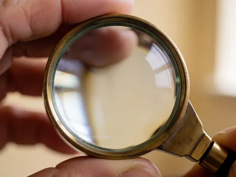 Close-up of a bronze-framed jeweler's loupe held by hands with a blurred workshop background for watch repair details