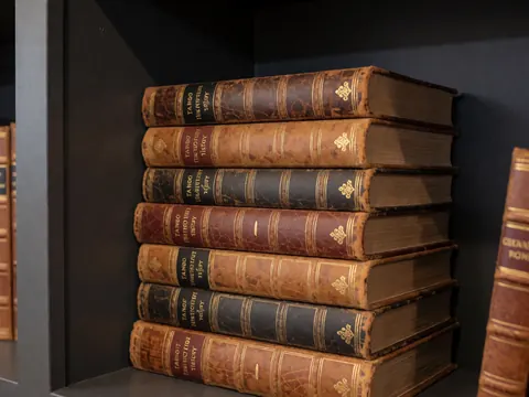 Stack of old books about tango history on a wooden shelf with gray carbon walls and warm professional lighting