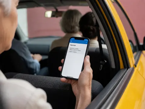 Close-up of a hand holding a smartphone inside a taxi, showing the screen with a translation app interface against a pink wall background.