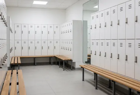 Clean locker room featuring white lockers, wooden benches, and mirrors, suitable for a gym or boxing center interior