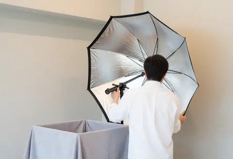 Portrait photographer adjusting an umbrella reflector next to a softbox with gray fabric in a studio with neutral walls and soft lighting.