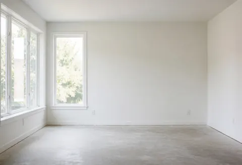 Empty interior space with concrete flooring and white walls, featuring large windows that let in natural light, suitable for cork flooring installation.