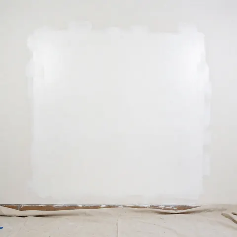 A white wall that has been repaired and is ready for painting, with protective sheeting on the floor, suitable for wall repair business details.