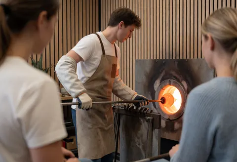 Glassblower working with molten glass in a workshop using a glory hole and wooden walls