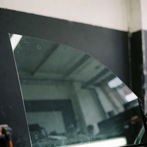 Clean car window with a single water droplet reflecting a workshop and black walls for vehicle washing service
