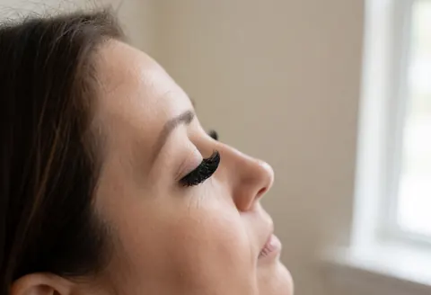 Close-up of eyes featuring dramatic false eyelashes with soft natural light and a blurred beige wall background in a beauty salon setting