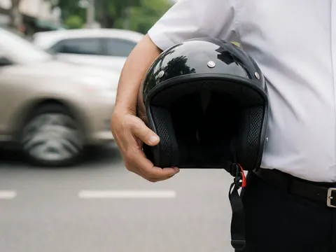Close-up of a hand holding a black motorcycle helmet with blurred cars in the background, highlighting safety gear for motorbike taxi services.