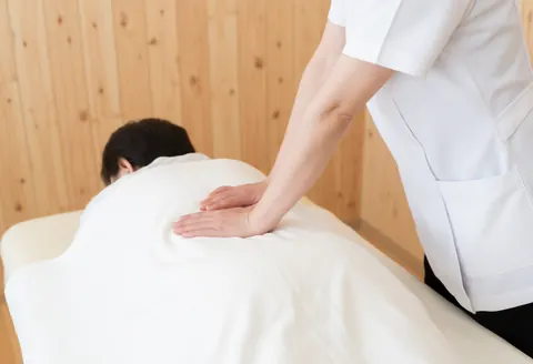 Therapist applying professional back massage to client using a white towel in a light wood room