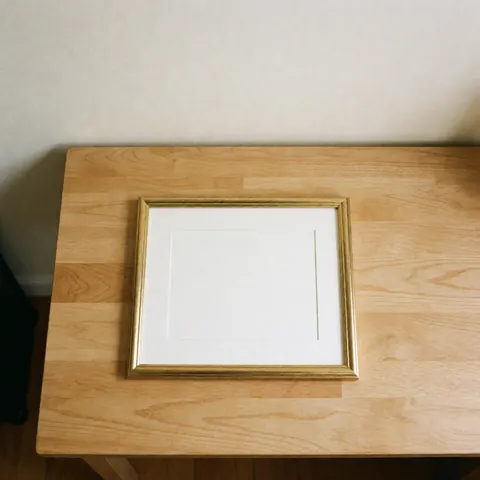 Golden diploma frame resting on a light wooden table against a warm white wall, presenting a clean and minimalist aesthetic suitable for graduation photography products.