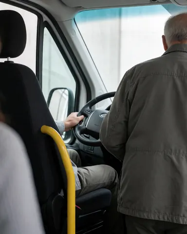 A passenger enters a minibus while the driver's hand rests on the steering wheel, with a yellow handrail and black seats visible inside.