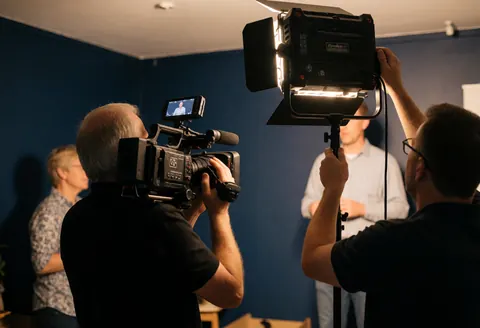 Videographer in action with cinema camera and LED light against blue walls, realistic scene useful for business