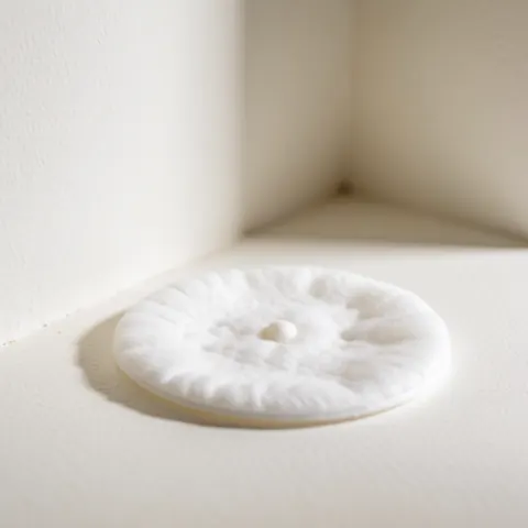 Close-up of a white cotton pad featuring a small black dot in the corner, highlighting texture for facial cleansing products
