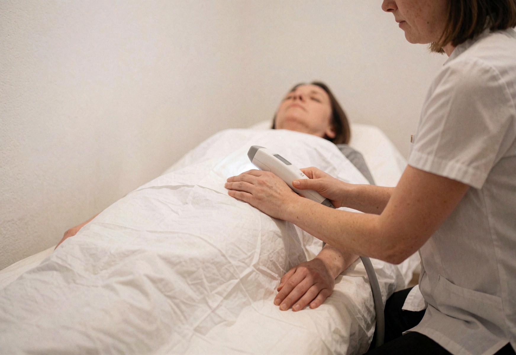 Professional performing laser hair removal on a client lying on a treatment table with a white drape in a clinic setting