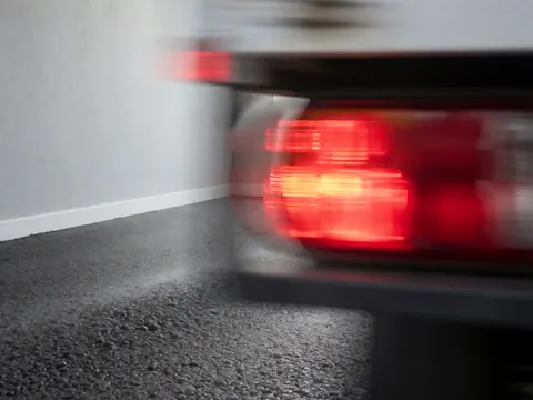 Blurred red taillights of a moving truck against gray walls and textured asphalt, capturing kinetic motion and speed effects.