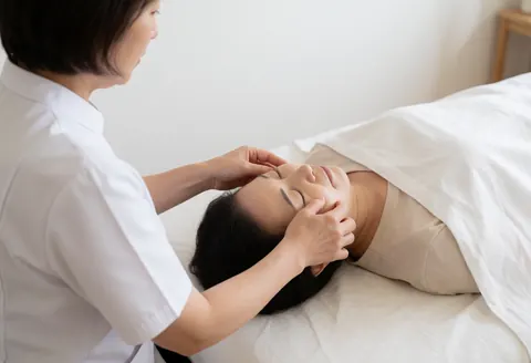 Shiatsu practitioner applying gentle hand pressure to a client's face during a relaxing facial massage session.