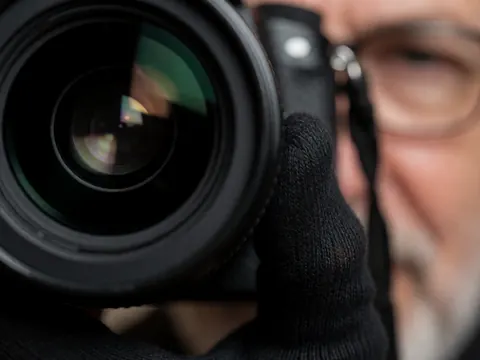 Close-up of a hand wearing a black glove pressing the shutter button on a professional camera lens with dramatic lighting and blurred background reflections