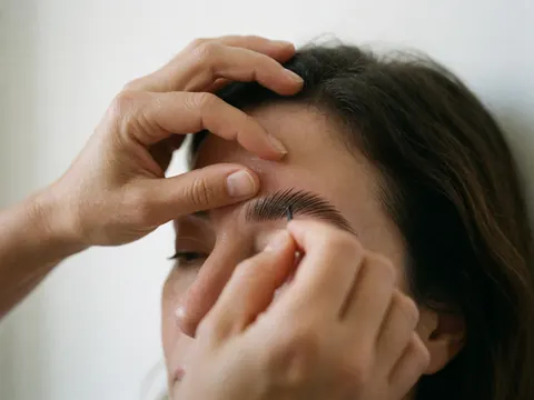 Close-up of a makeup artist using a brush to apply lamination product to an eyebrow during a beauty service