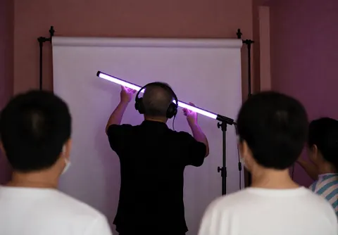Graduation photographer adjusting a purple LED light in a studio with pink walls and a white backdrop