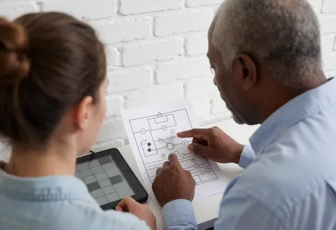 Chess coach and student reviewing a game diagram at a chess school with a white brick wall background