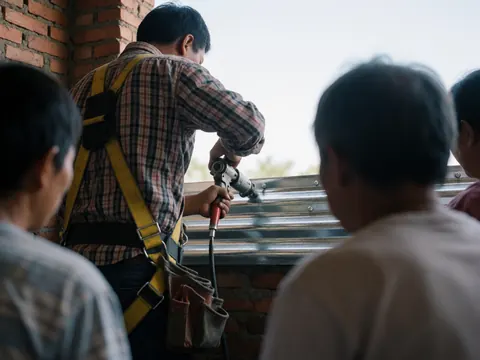 Worker wearing safety harness riveting corrugated zinc sheet against brick wall during heating repair service
