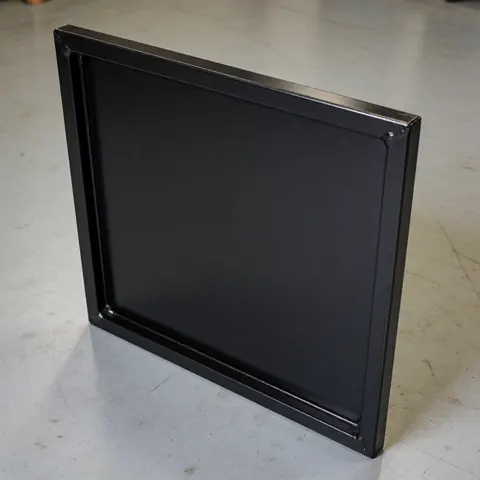 Close-up of a black matte painted metal repair panel showing welded seams on a concrete workshop floor.