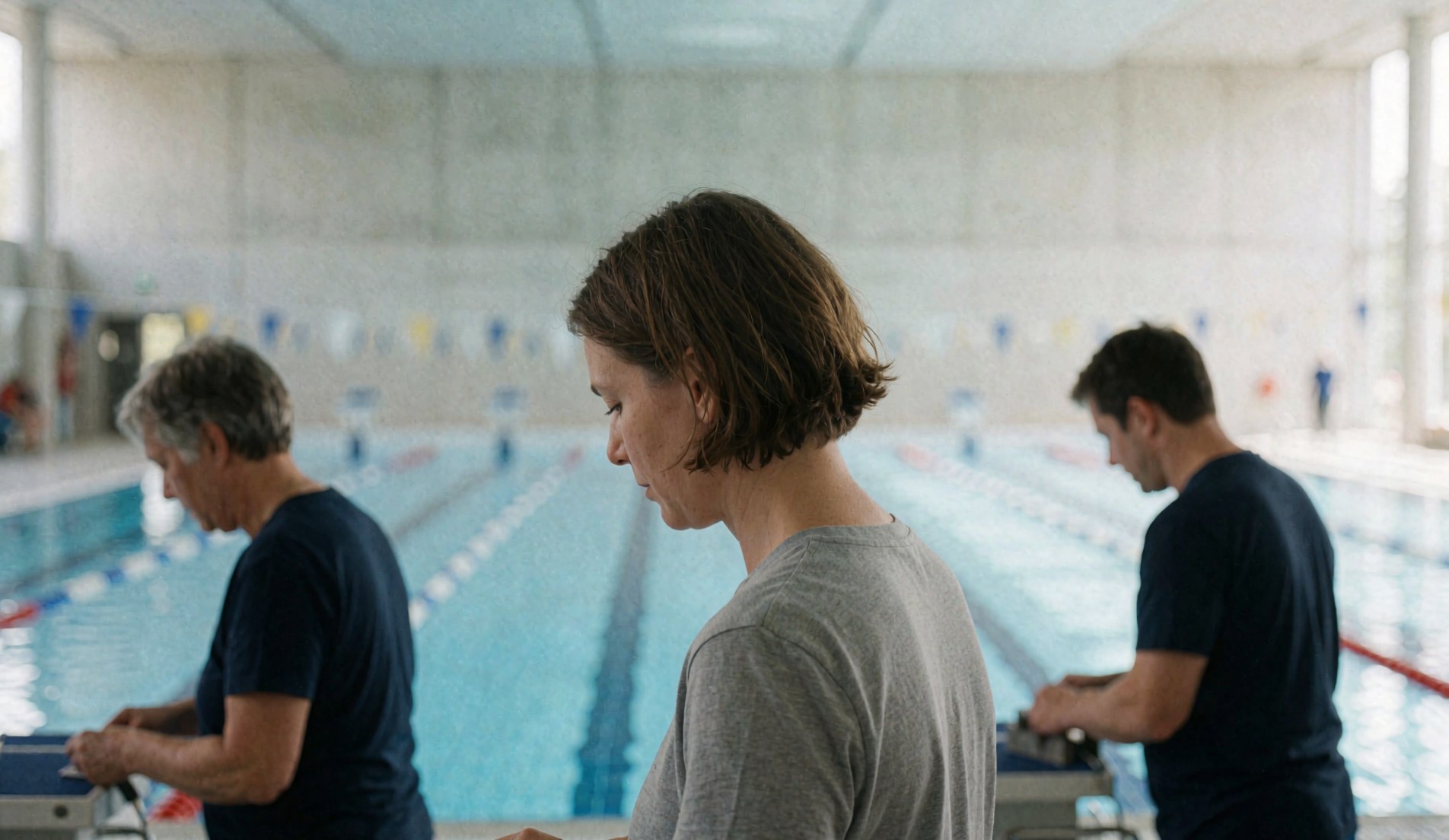 Coaches working with swimmers in a blue water Olympic pool featuring concrete walls and marked lanes for training.