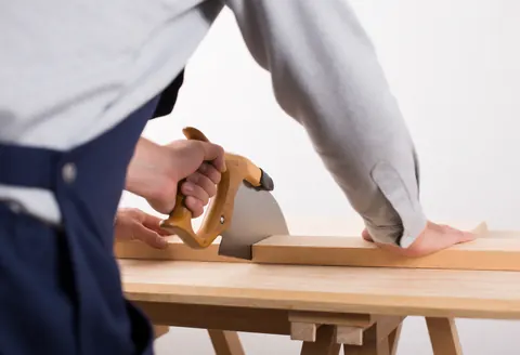 A worker uses a saw to cut wood in a carpentry workshop, demonstrating hands-on service in action.
