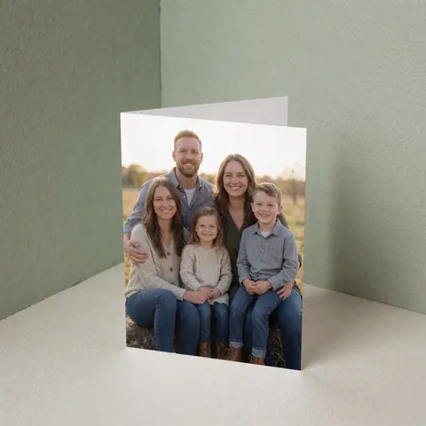 A family portrait displayed on a greeting card, set against a soft sage green wall with gentle lighting.