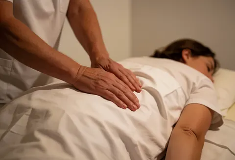 Close-up view of therapist's hands massaging a client's back on a white table in a bright spa setting.
