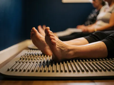 Close-up view of feet placed on a textured reflexology mat in a treatment room with blue walls.