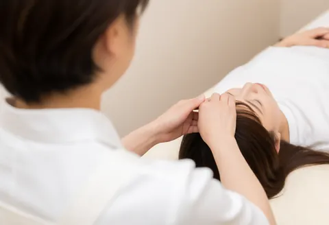 Professional therapist applying a head massage to a resting client on a treatment table.