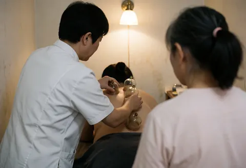 A therapist places suction cups on a client's back while another person observes in a warm professional setting.
