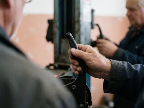 Close-up of a mechanic's hand gripping a bicycle brake lever during repair work in a workshop with soft lighting and blurred background.