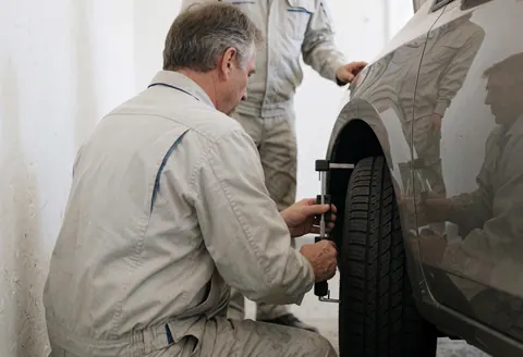 A mechanic uses a tool to measure tire tread depth in a white-walled auto repair shop during a vehicle inspection service.