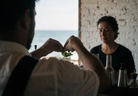 Close-up of a bartender placing a sprig of fresh mint into a cocktail drink at a beachside bar setting.