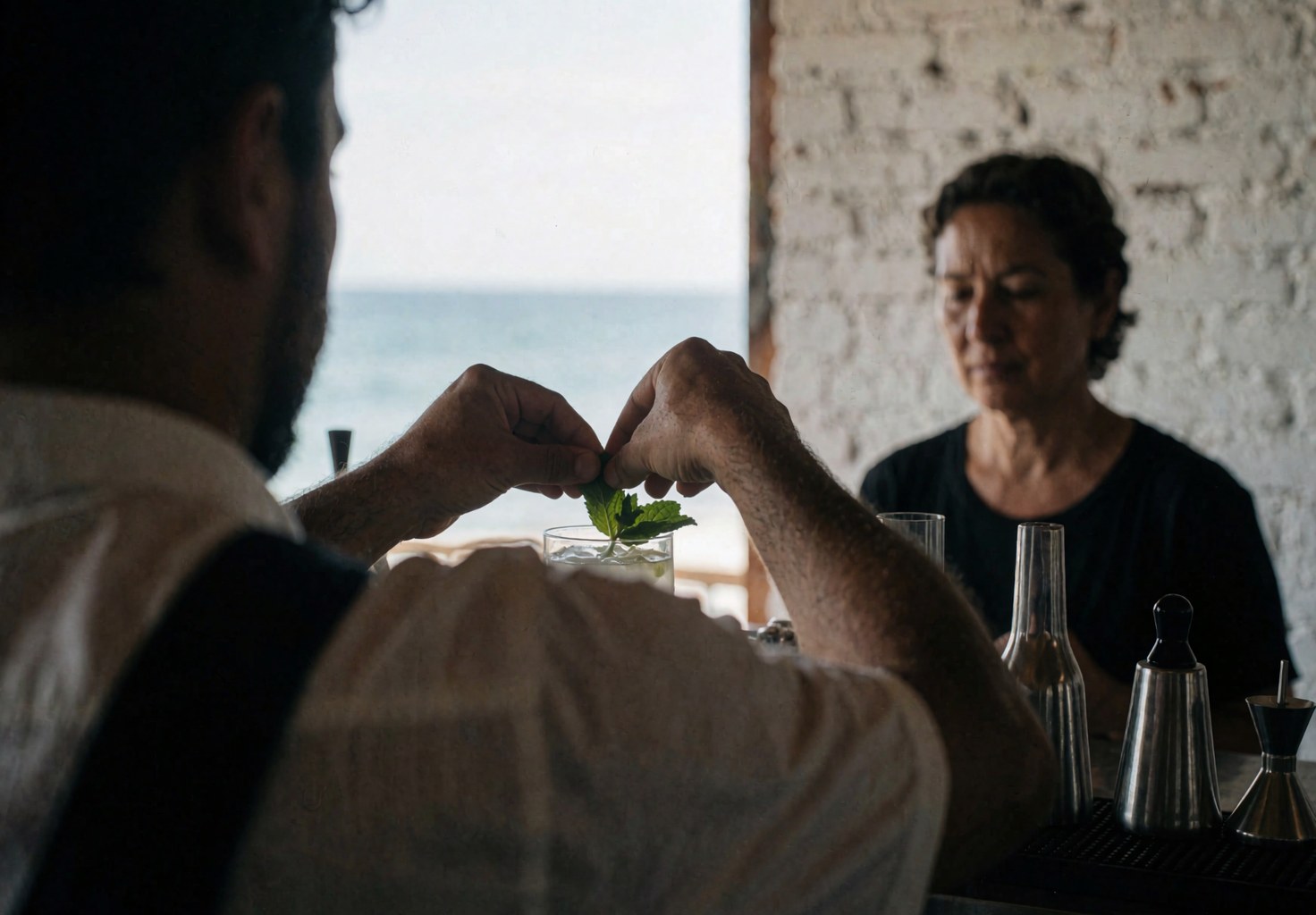 Close-up of a bartender placing a sprig of fresh mint into a cocktail drink at a beachside bar setting.