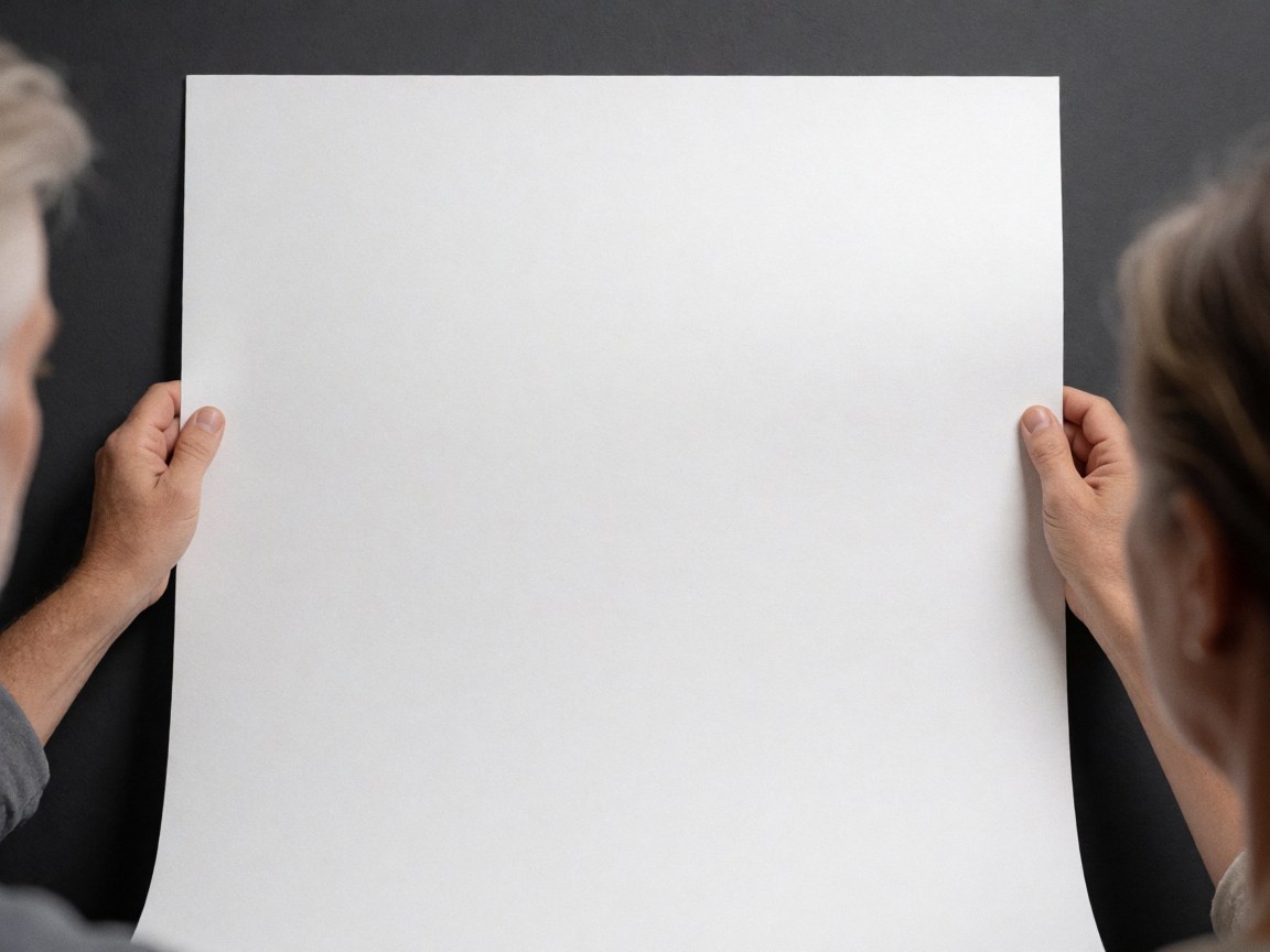 Hands holding a sheet of white paper against a gray wall, providing a clean background ideal for product presentation and graphic design layouts.