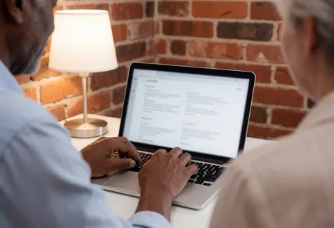 Close-up view of hands typing on a laptop keyboard in an office setting with warm lighting and exposed brick walls, suitable for online store websites.