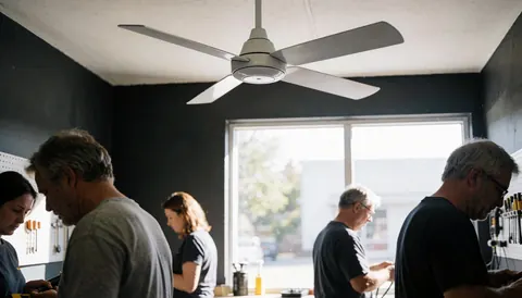 Technician repairing a white fan in a workshop with gray walls, natural light, and tools on the wall.