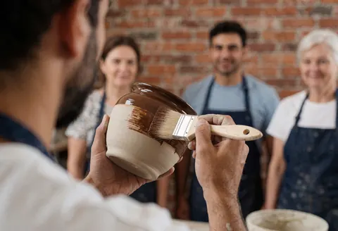 Close-up of hands using a brush to apply glaze to a ceramic bowl during a pottery workshop session.
