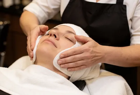 Therapist hands placing a warm steam compress on a client's face during a relaxing spa treatment session.