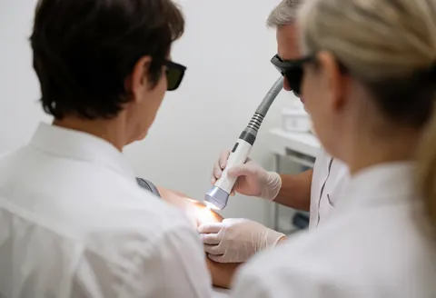 A technician wearing protective eyewear applies a laser skin treatment to a client in a clinical beauty center.