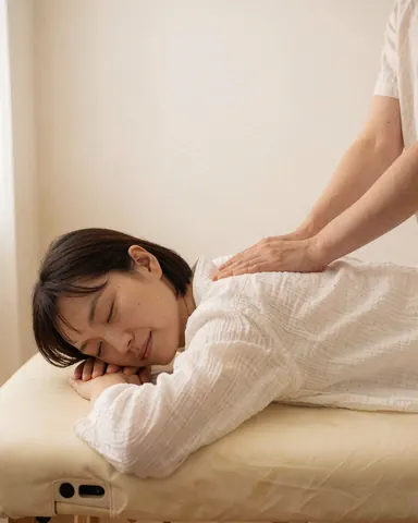 A Thai massage practitioner performs a treatment on a client lying face down on a white table in a calm setting.