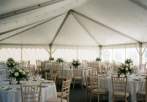 Interior view of a wedding banquet hall featuring round tables, wooden chairs, and white floral centerpieces ready for celebration.