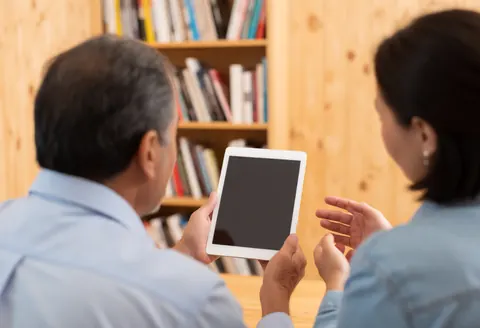 A documentary photographer holds a tablet while consulting with a client in a professional setting with a warm atmosphere.