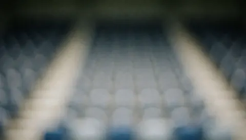 Out-of-focus stadium seating with a blue and gray gradient bokeh effect, suitable for soccer coach text overlays.