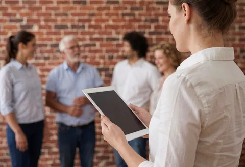 A woman holding a tablet speaks to a group in front of a brick wall, illustrating wedding planning services.