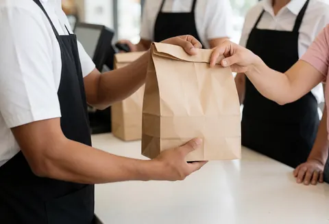 Staff member hands a food bag to a customer at a clean modern counter in a professional restaurant setting