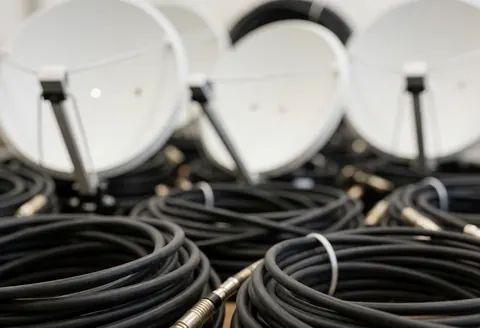 White satellite dishes and coiled coaxial cables stored in a warehouse for antenna installation services