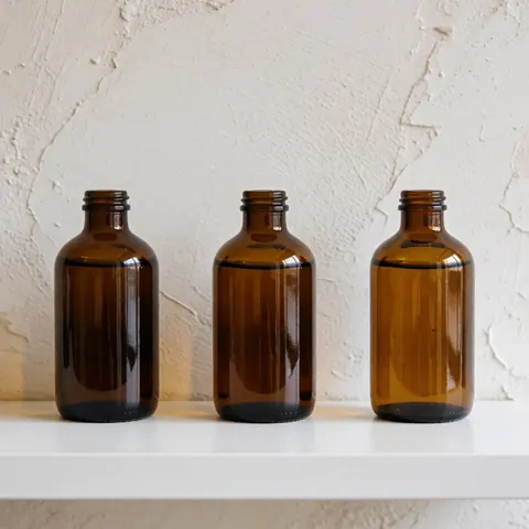 Three brown glass bottles of cervical massage oil arranged on a white shelf against a textured wall with natural lighting for a wellness clinic